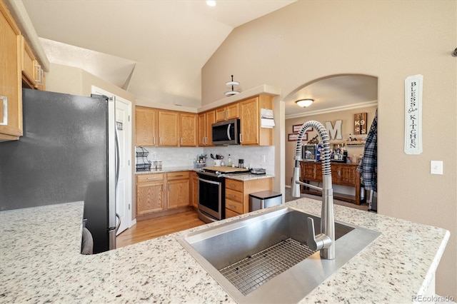 56330 E 37th Ct, Strasburg, CO 80136 - kitchen with stainless steel appliances, arched walkways, a sink, light wood-style floors, and decorative backsplash
