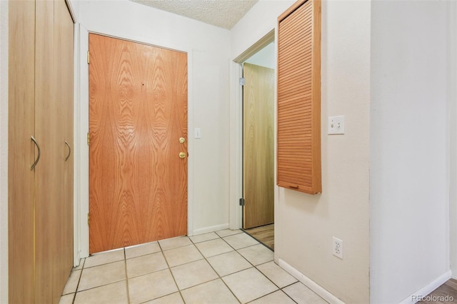 corridor with baseboards, a textured ceiling, and light tile patterned floors