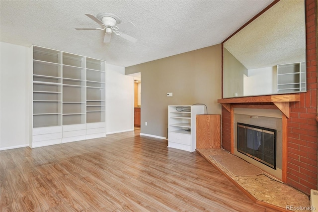 unfurnished living room with a textured ceiling, baseboards, a glass covered fireplace, a ceiling fan, and wood finished floors