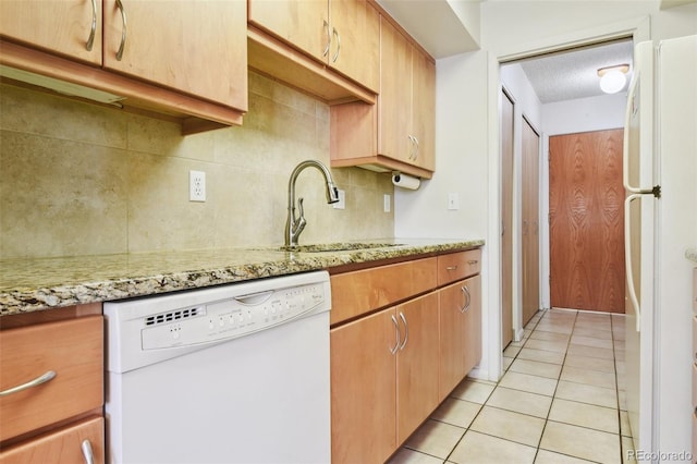 kitchen with light stone counters, a sink, white appliances, light tile patterned floors, and backsplash