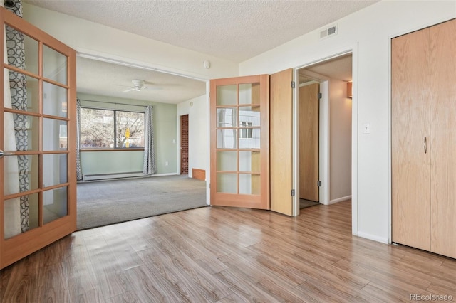 spare room featuring light wood finished floors, a textured ceiling, baseboards, visible vents, and baseboard heating