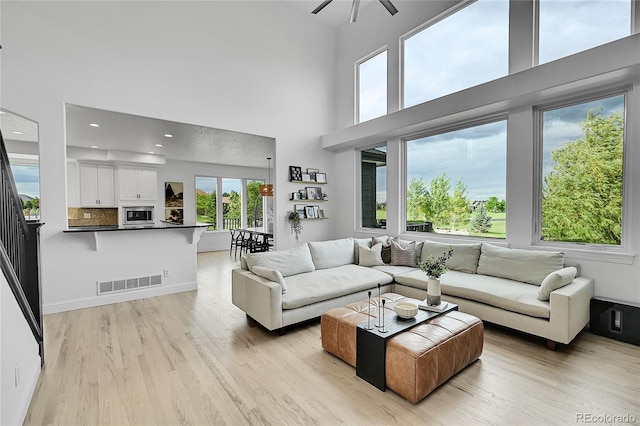 living area with light wood-type flooring, a towering ceiling, a ceiling fan, and recessed lighting