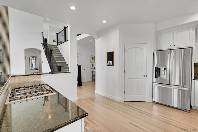 kitchen with appliances with stainless steel finishes, arched walkways, light wood-type flooring, dark stone counters, and recessed lighting