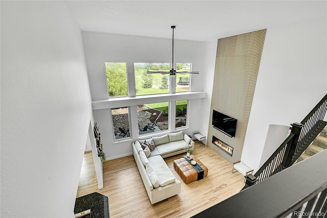 living room with a ceiling fan, a large fireplace, wood finished floors, stairs, and baseboards