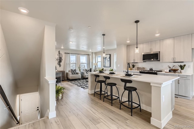 kitchen featuring light hardwood / wood-style floors, a breakfast bar area, an island with sink, pendant lighting, and range with gas cooktop