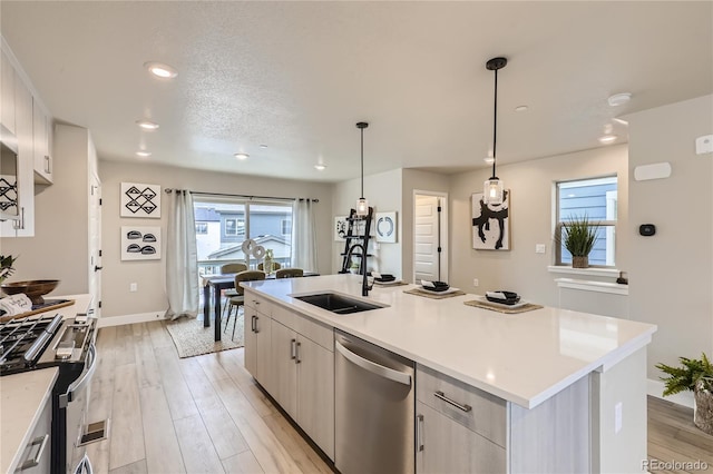 kitchen with a center island with sink, white cabinetry, light hardwood / wood-style flooring, stainless steel appliances, and decorative light fixtures