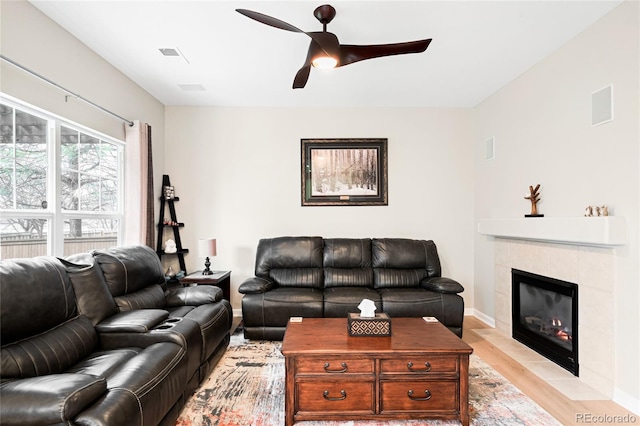living area featuring light wood finished floors, a ceiling fan, a tiled fireplace, and baseboards
