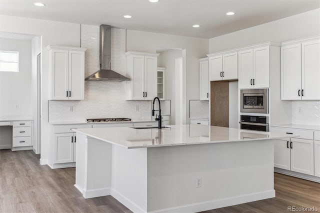 kitchen with stainless steel appliances, white cabinetry, a kitchen island with sink, and wall chimney exhaust hood