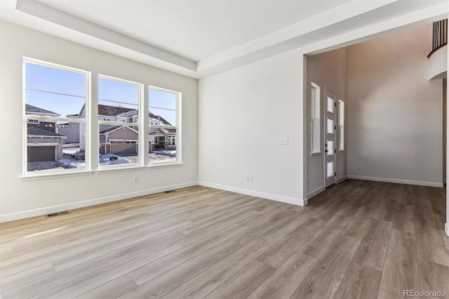 empty room with a tray ceiling and light wood-type flooring