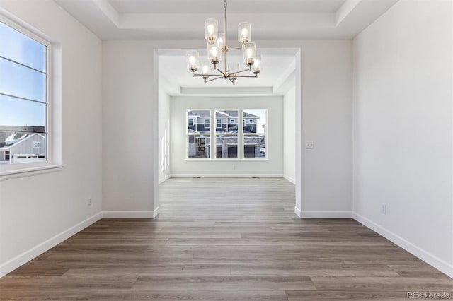 unfurnished dining area featuring a raised ceiling, hardwood / wood-style flooring, and a chandelier