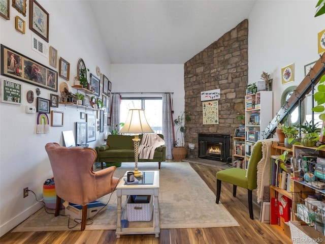 living room featuring hardwood / wood-style flooring, a stone fireplace, and high vaulted ceiling