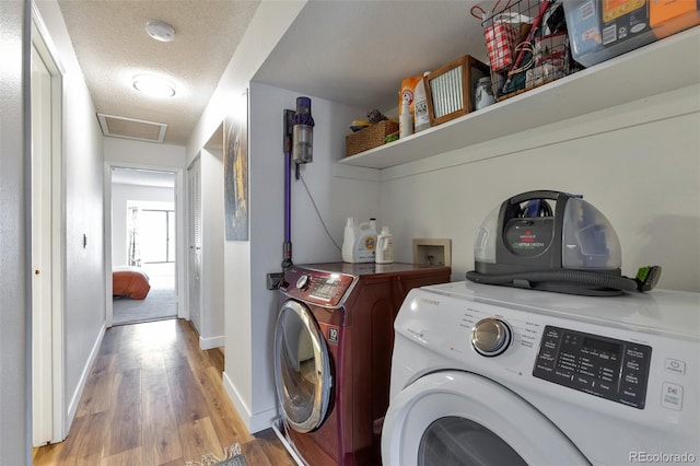 laundry room featuring washing machine and clothes dryer, a textured ceiling, and light hardwood / wood-style flooring