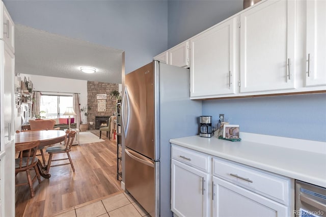 kitchen with stainless steel fridge, a textured ceiling, white cabinets, a stone fireplace, and light wood-type flooring