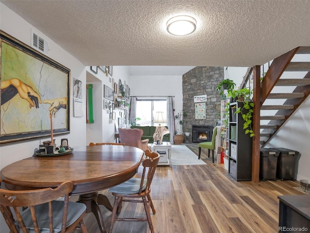 dining space with wood-type flooring, a stone fireplace, and a textured ceiling