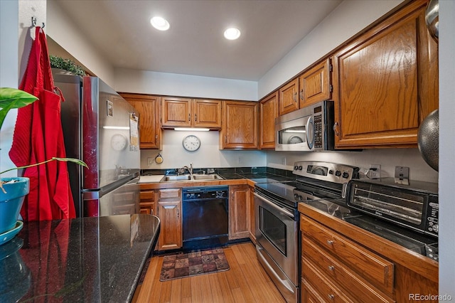 31270 John Wallace Rd Unit 310, Evergreen, CO 80439 - kitchen with stainless steel appliances, brown cabinetry, a sink, light wood finished floors, and dark countertops