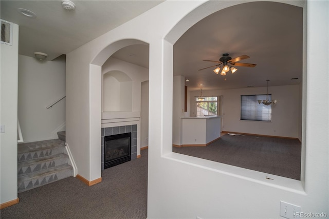 unfurnished living room with a tiled fireplace, carpet floors, and ceiling fan with notable chandelier