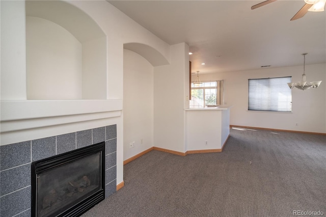 unfurnished living room with ceiling fan with notable chandelier, a tiled fireplace, and dark colored carpet