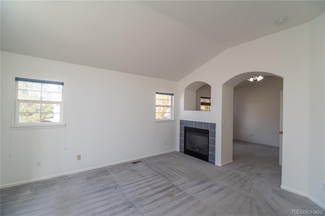 unfurnished living room featuring lofted ceiling, a tile fireplace, and light colored carpet