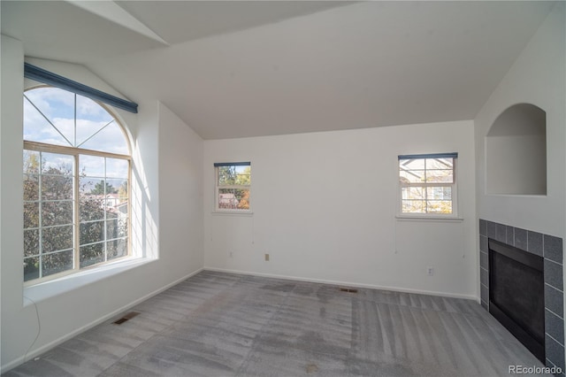 unfurnished living room with carpet floors, a tile fireplace, plenty of natural light, and vaulted ceiling