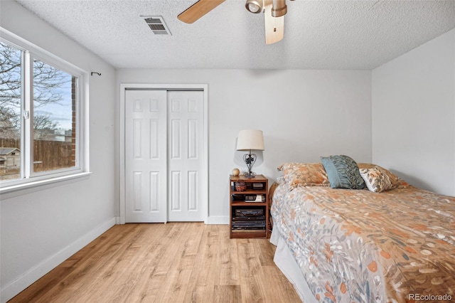 bedroom with ceiling fan, light hardwood / wood-style floors, a textured ceiling, and a closet