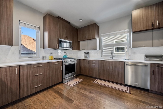 kitchen with sink, a wealth of natural light, dark hardwood / wood-style floors, decorative backsplash, and stainless steel appliances