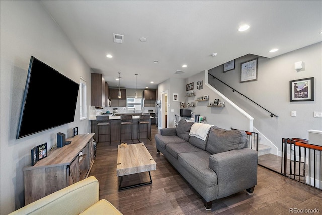 living room featuring recessed lighting, dark wood finished floors, and stairs