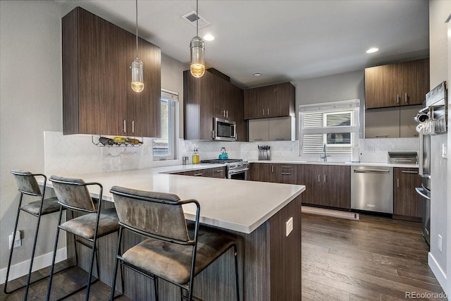 kitchen with visible vents, dark wood-type flooring, tasteful backsplash, stainless steel appliances, and a peninsula