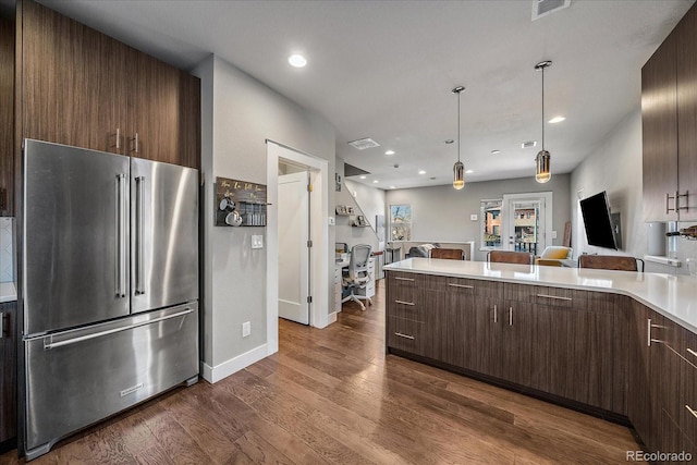 kitchen with dark brown cabinets, dark wood-type flooring, high end fridge, and light countertops