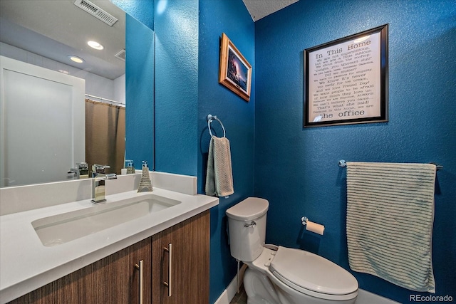 full bathroom featuring visible vents, toilet, vanity, and a textured wall