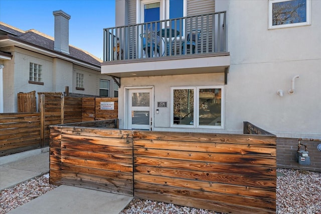 back of house featuring a balcony, fence, and stucco siding