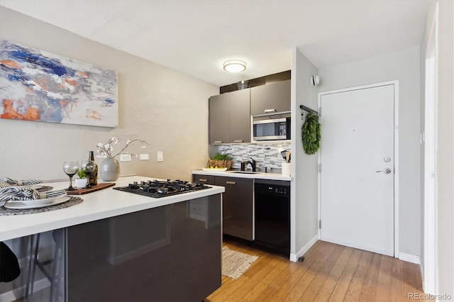 kitchen with black appliances, sink, decorative backsplash, kitchen peninsula, and light hardwood / wood-style flooring