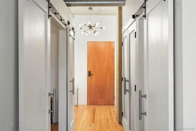 hallway with a barn door, light wood-type flooring, and a chandelier