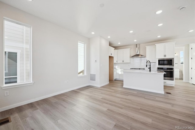 kitchen featuring a kitchen island with sink, white cabinets, oven, wall chimney range hood, and built in microwave