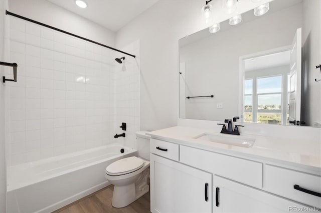 full bathroom featuring hardwood / wood-style flooring, tiled shower / bath combo, toilet, and vanity