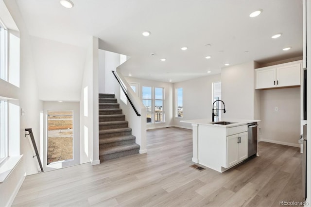 kitchen with white cabinets, sink, dishwasher, light hardwood / wood-style floors, and an island with sink