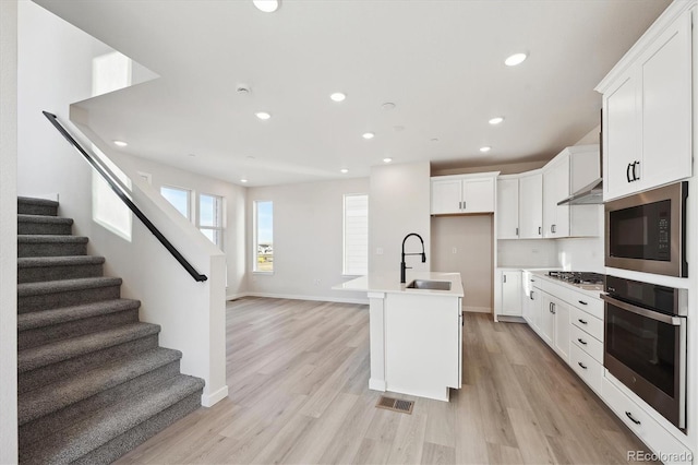 kitchen featuring sink, light wood-type flooring, an island with sink, white cabinetry, and stainless steel appliances