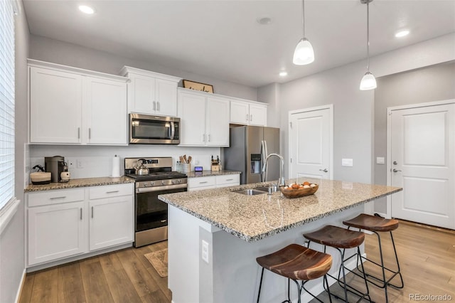 kitchen with a breakfast bar area, appliances with stainless steel finishes, white cabinets, an island with sink, and light wood-type flooring