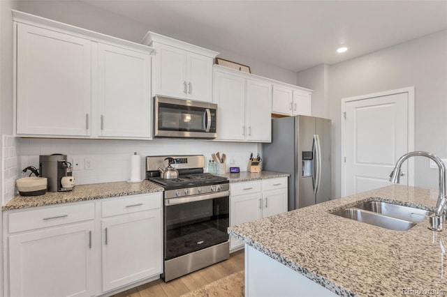 kitchen with stainless steel appliances, white cabinetry, sink, and light hardwood / wood-style flooring