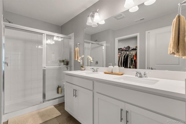 bathroom with double vanity, a shower stall, visible vents, and a sink