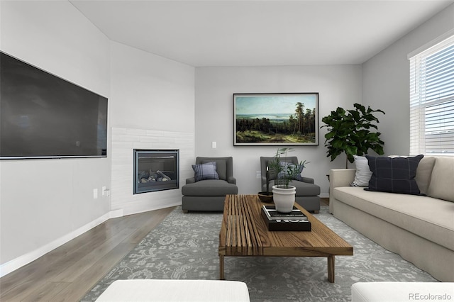 living room with a glass covered fireplace, wood finished floors, and baseboards