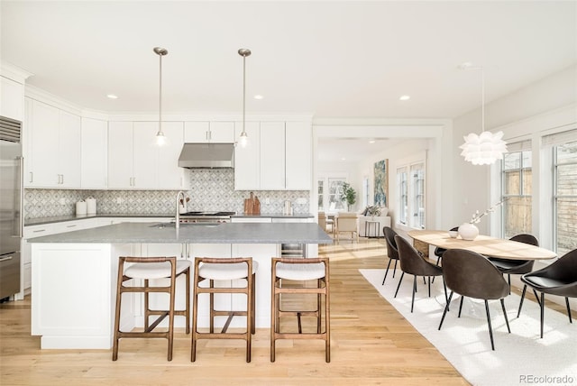 kitchen with a kitchen island with sink, backsplash, decorative light fixtures, and white cabinets