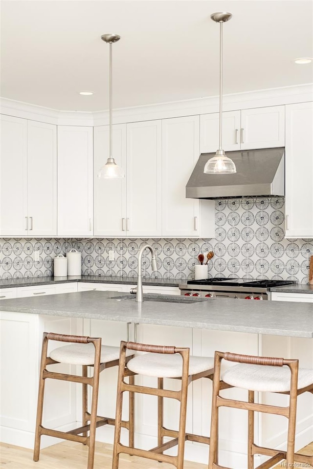 kitchen featuring a breakfast bar, white cabinetry, stove, ventilation hood, and decorative light fixtures