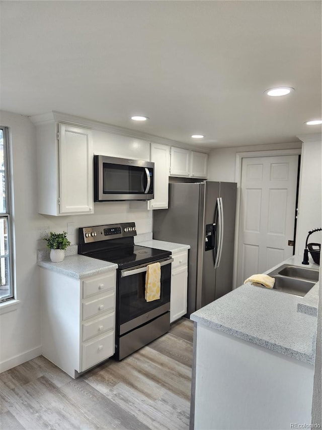 kitchen with light wood finished floors, recessed lighting, a sink, stainless steel appliances, and white cabinetry