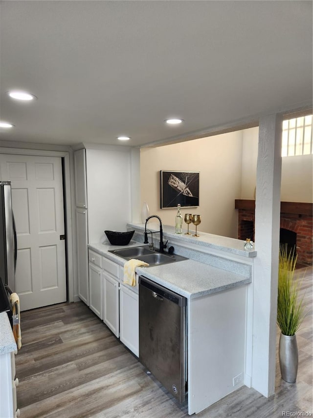 kitchen featuring a fireplace, a sink, light wood-style floors, appliances with stainless steel finishes, and white cabinetry