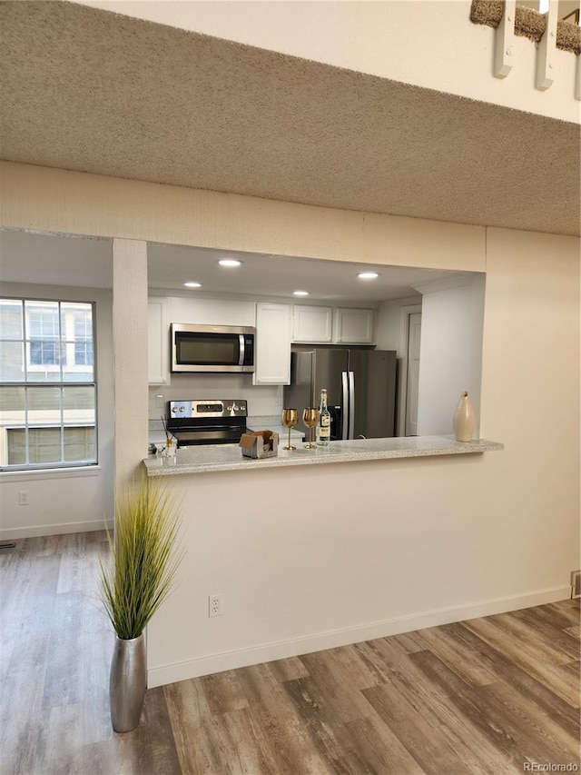 kitchen with baseboards, light countertops, wood finished floors, white cabinets, and stainless steel appliances