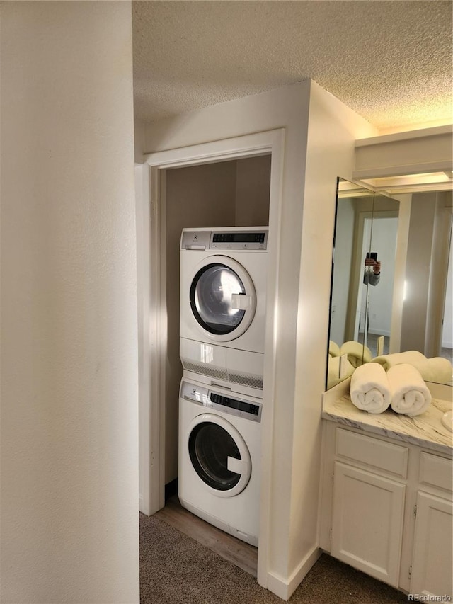 clothes washing area featuring a textured ceiling and stacked washing maching and dryer