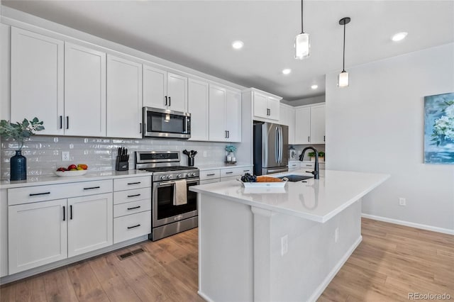 kitchen with appliances with stainless steel finishes, sink, white cabinetry, and a center island with sink