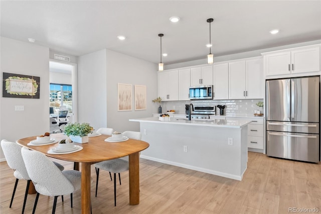 kitchen featuring backsplash, hanging light fixtures, appliances with stainless steel finishes, and a kitchen island with sink