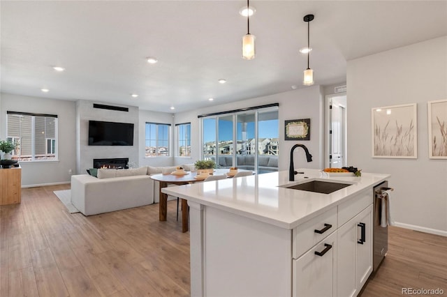 kitchen with white cabinets, decorative light fixtures, a fireplace, sink, and a kitchen island with sink