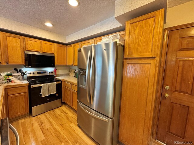 971 S Evanston Cir, Aurora, CO 80012 - kitchen with stainless steel appliances, a textured ceiling, light countertops, light wood-style floors, and brown cabinets